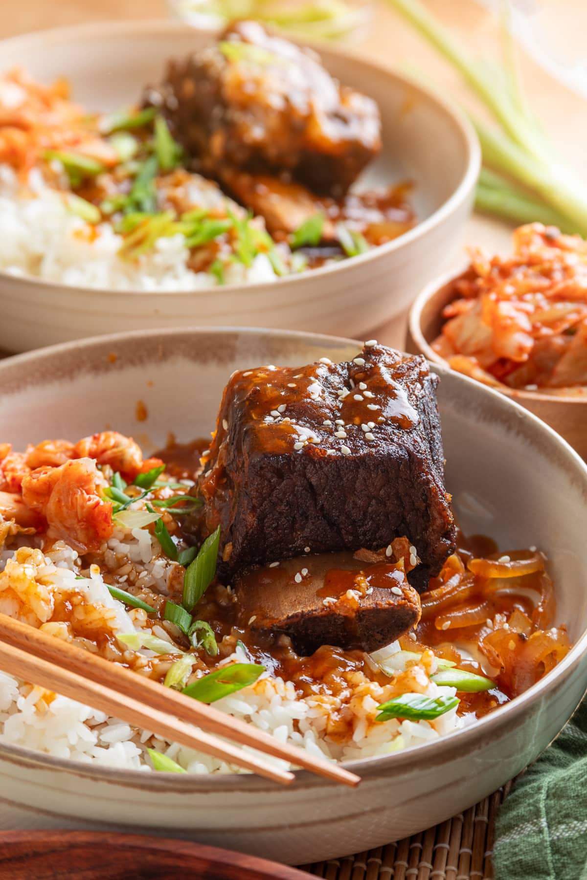 Korean Braised Short Ribs Rice Bowls with Kimchi Korean braised short ribs over white rice with gochujang sauce, softened onions, green onions, sesame seeds, and kimchi.