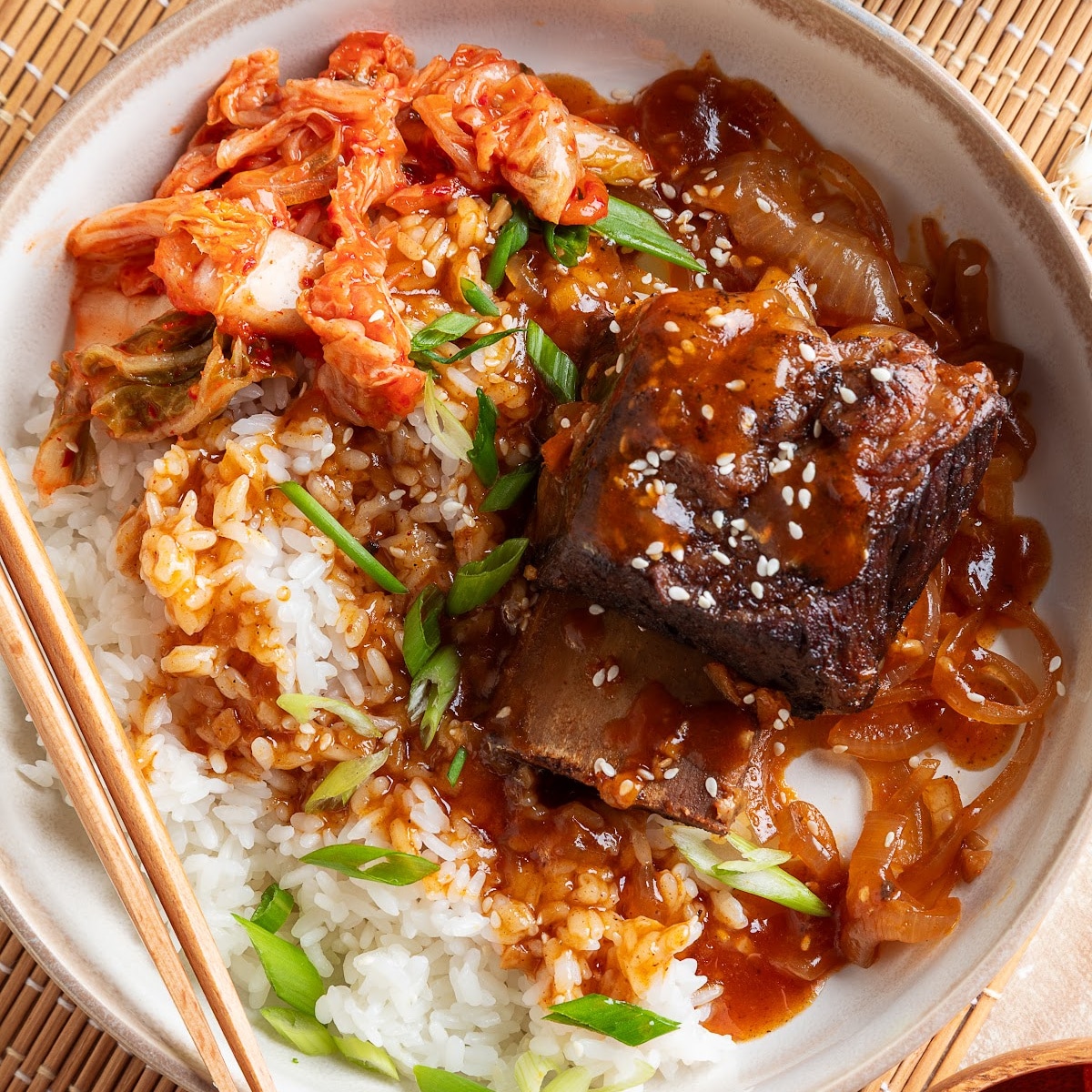 Bone-in Korean braised short rib served over steamed white rice with softened onions, gochujang sauce, kimchi, and green onions.