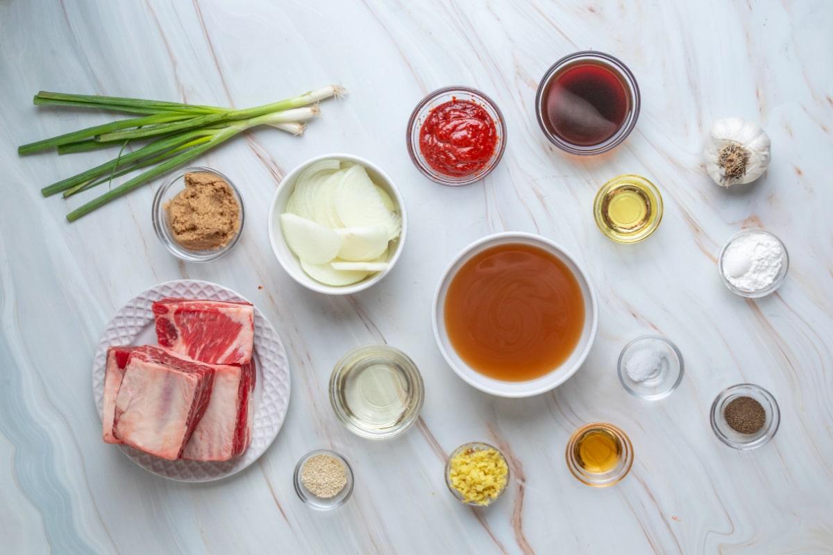 Ingredients for Slow Cooker Korean Braised Short Ribs Ingredients for Korean braised short ribs, including bone-in beef, gochujang, brown sugar, ginger, garlic, soy sauce, beef stock, and onions.