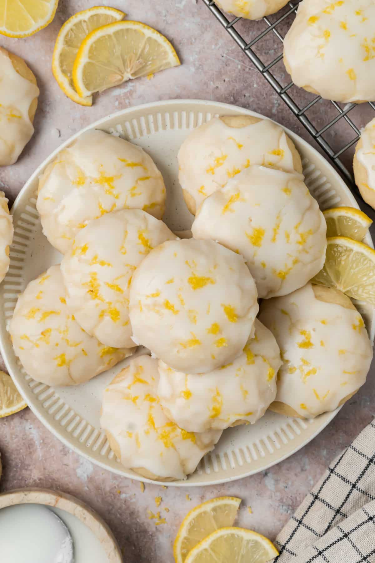 Lemon glazed ricotta cookies topped with fresh zest on a serving plate with sliced lemons