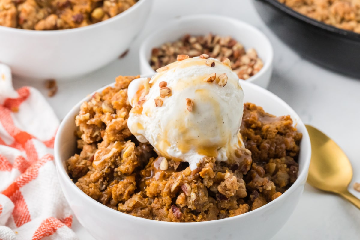 Creamy pumpkin filling with golden oat topping, melting vanilla ice cream, caramel sauce, and chopped pecans. Bowl of pumpkin crisp with buttery oat and pecan topping, vanilla ice cream, and caramel drizzle.