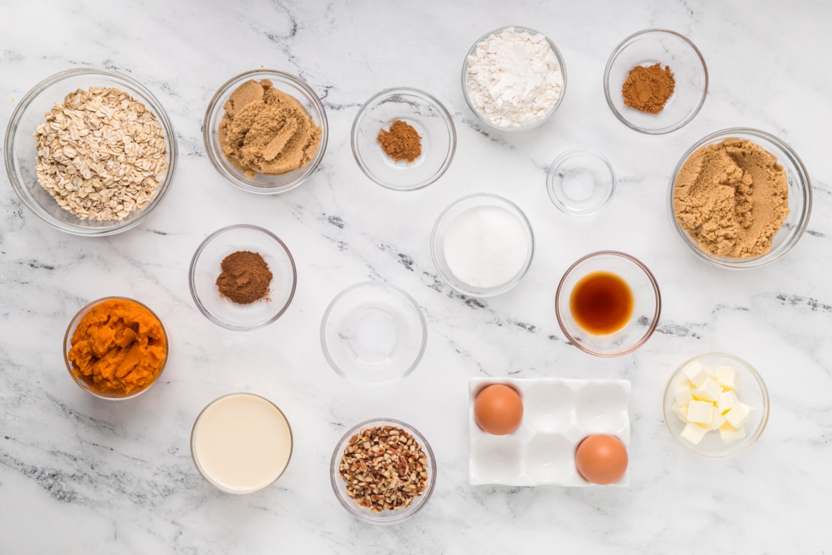 Pumpkin purée, oats, chopped pecans, sugars, butter, eggs, and warm spices measured out for pumpkin crisp. Ingredients for homemade pumpkin crisp, including pumpkin purée, rolled oats, pecans, brown sugar, butter, eggs, evaporated milk, and spices.