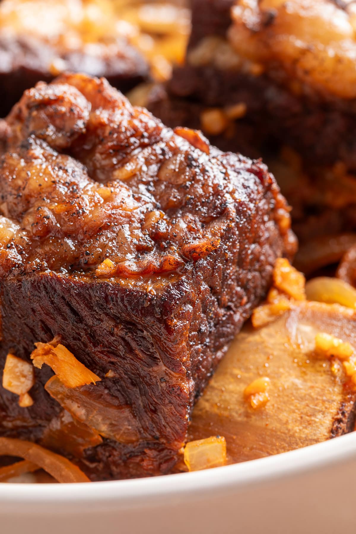 Tender Bone-In Beef Short Ribs After Slow Cooking Close-up of tender bone-in beef short ribs with a dark brown exterior, softened onions, and sauce.